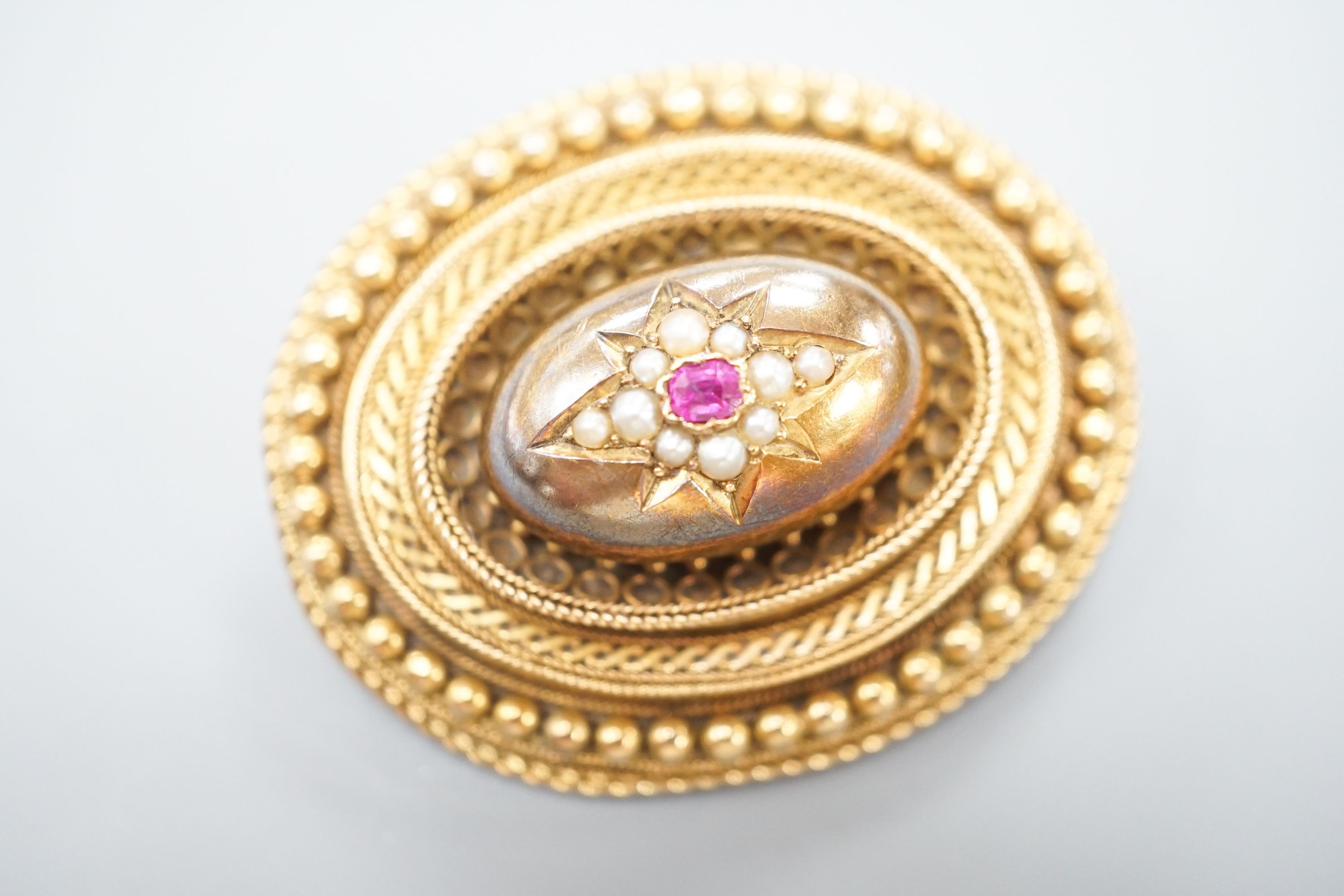 A Victorian yellow metal, ruby? and seed pearl set oval brooch, with glazed back, 43mm, gross weight 18.7 grams.